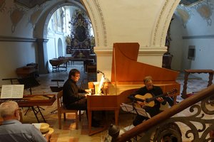 Ein Kirchenraum in welchem eine Person an einem Flügel spielt und eine weitere Person mit eine akustischen Gitarre. 