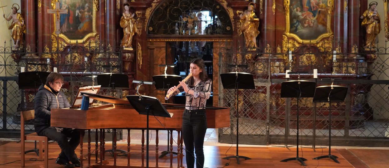 Eine Person spielt Klavier und eine andere Person spielt Flöte in einer Kirche. 